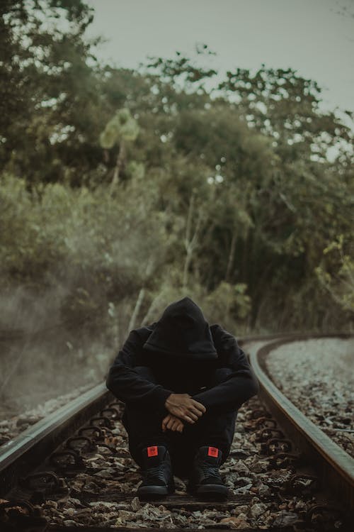 A depressed hooded man sitting alone outdoors. Social Isolation and Poor Mental Health